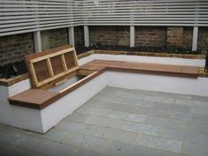 a wooden bench sitting on top of a stone floor next to a brick wall and planters