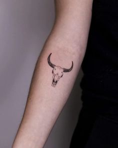 a woman's arm with a tattoo of a bull skull on the left forearm