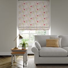 a living room with a couch, table and window covered in floral roman blind shades