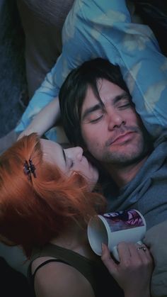 a man laying next to a woman on top of a bed while holding a cup