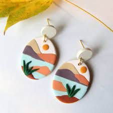 a pair of earrings sitting on top of a white table next to a yellow leaf