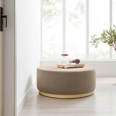 a living room with a round ottoman in front of a window and potted plant