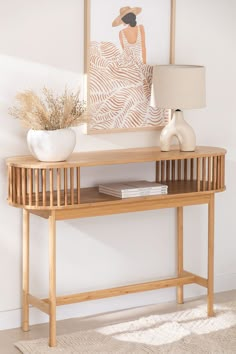 a wooden table with a lamp and vase on it next to a wall mounted painting