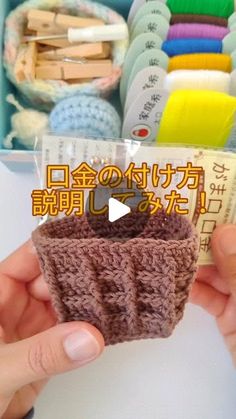 someone holding up a small crocheted cup in front of a box of yarns