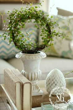 a white vase filled with green plants on top of a table next to a book