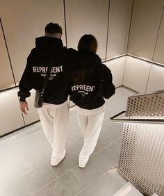 two people wearing black sweatshirts walking down an escalator in a public building