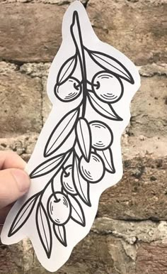 someone holding up a sticker with olives and leaves on it in front of a brick wall