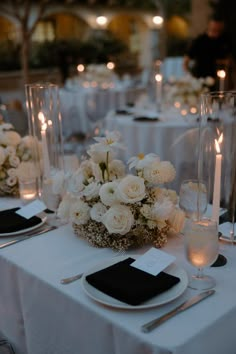 the table is set with white flowers and black napkins, silverware and candles