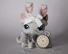 a small toy cat with bunny ears holding an alarm clock in front of it's face