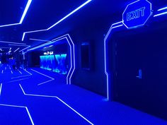 an exit sign lit up at night in a hallway with neon lights and blue carpet