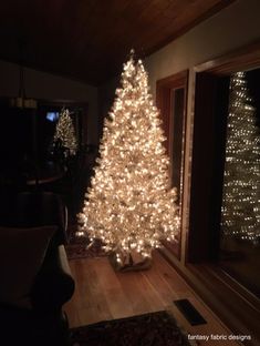 a white christmas tree is lit up in front of a window with lights on it