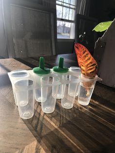 six plastic cups sitting on top of a wooden table next to an orange and green leaf