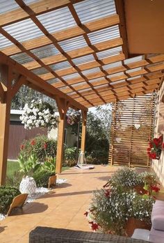 a patio covered in lots of flowers and greenery next to a wall with wooden slats on it