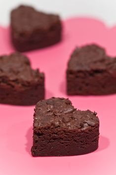 four pieces of chocolate brownie on a pink surface with hearts shaped in the middle