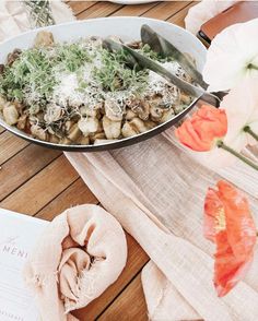 a bowl filled with food sitting on top of a wooden table next to flowers and napkins