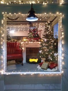 a christmas tree is in the reflection of a window with lights on it and a red chair