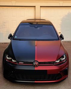 the front end of a red and black car parked in front of a garage door