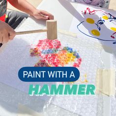 two children are painting with hammers on a sheet of white paper that says paint with a hammer