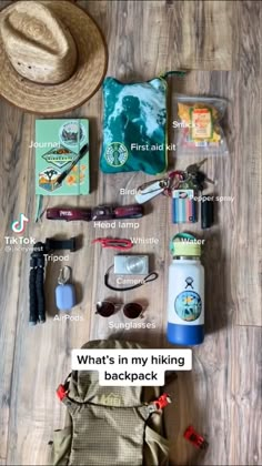 the contents of a backpack laid out on top of a wooden floor next to a hat and sunglasses