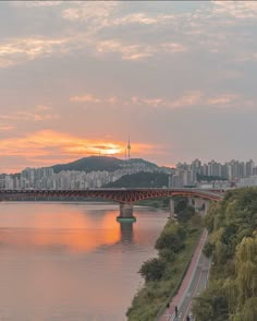 the sun is setting over a river with a bridge in the foreground and buildings on the other side