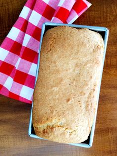 a loaf of bread sitting in a blue box on top of a wooden table next to a red and white checkered napkin