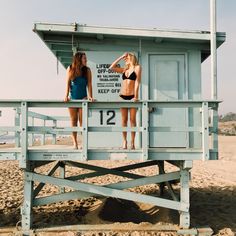 two women in bathing suits standing on a lifeguard tower