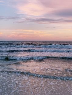 the ocean waves are rolling in to shore at sunset or dawn with pink and blue colors