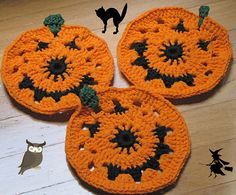 three crocheted pumpkin coasters on a wooden table with a black cat standing next to them