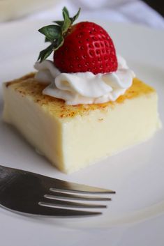 a piece of cheesecake with whipped cream and a strawberry on top sits on a plate next to a fork