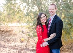 a man and woman standing next to each other in front of some trees with their arms around each other