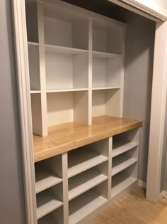 an empty room with white shelves and wood flooring on the walls, in front of a gray wall