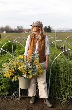 a woman standing in a garden holding a bucket full of flowers