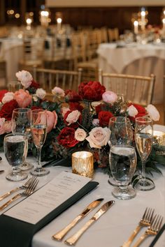 the table is set with silverware and red flowers in vases, gold rimmed glasses