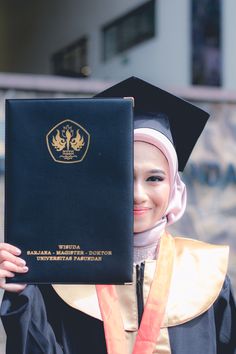 a woman in a graduation gown holding up a book with an emblem on the front