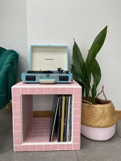 a record player sitting on top of a pink shelf next to a potted plant