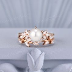 a white pearl and diamond ring on top of a white cloth with a flower design