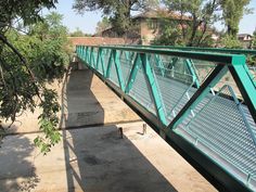 a green pedestrian bridge over a river next to trees