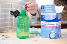 a woman holding a green bottle next to a carton of denture cleanser