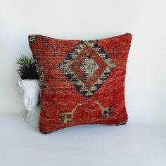 a decorative pillow on a white table next to a vase with a plant in it