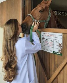 a woman in white shirt kissing a horse on the nose while wearing a green bridle