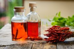 two bottles filled with liquid sitting on top of a wooden table next to some herbs