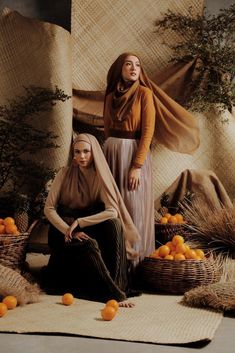 two women sitting on the ground surrounded by oranges