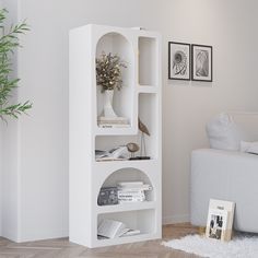 a living room with a white couch and book shelf in the corner next to a plant