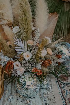 an arrangement of flowers, feathers and disco ball on a table with a mirror ball