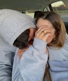 two women in hoodies are hugging each other while sitting in the back seat of a car