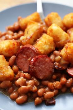 a blue plate topped with beans, sausage and tater tots next to a fork