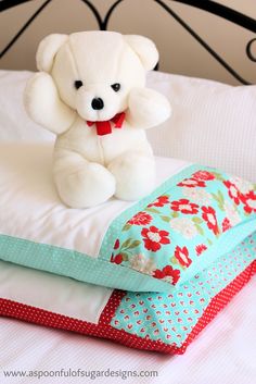 a white teddy bear sitting on top of a bed next to pillows and pillow cases