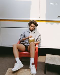 a woman sitting on a red chair in front of a white and yellow bus with her legs crossed