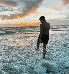 a man walking into the ocean at sunset