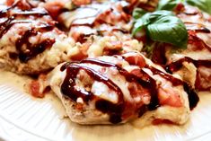 a white plate topped with meat covered in sauce and garnished with green leaves